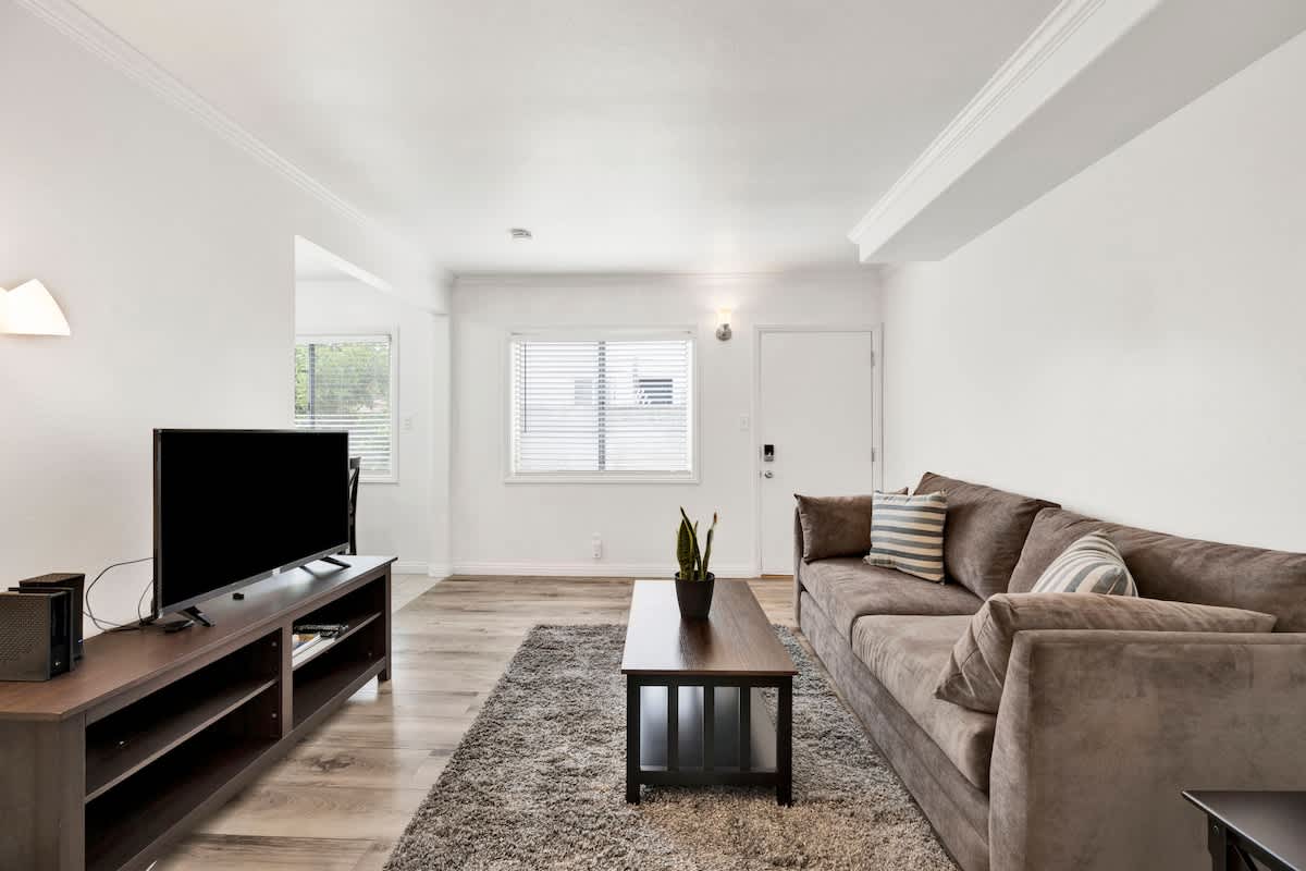 Bright living room in one of our furnished short term rentals in Santa Monica featuring a cream sofa, wooden table, and natural light.